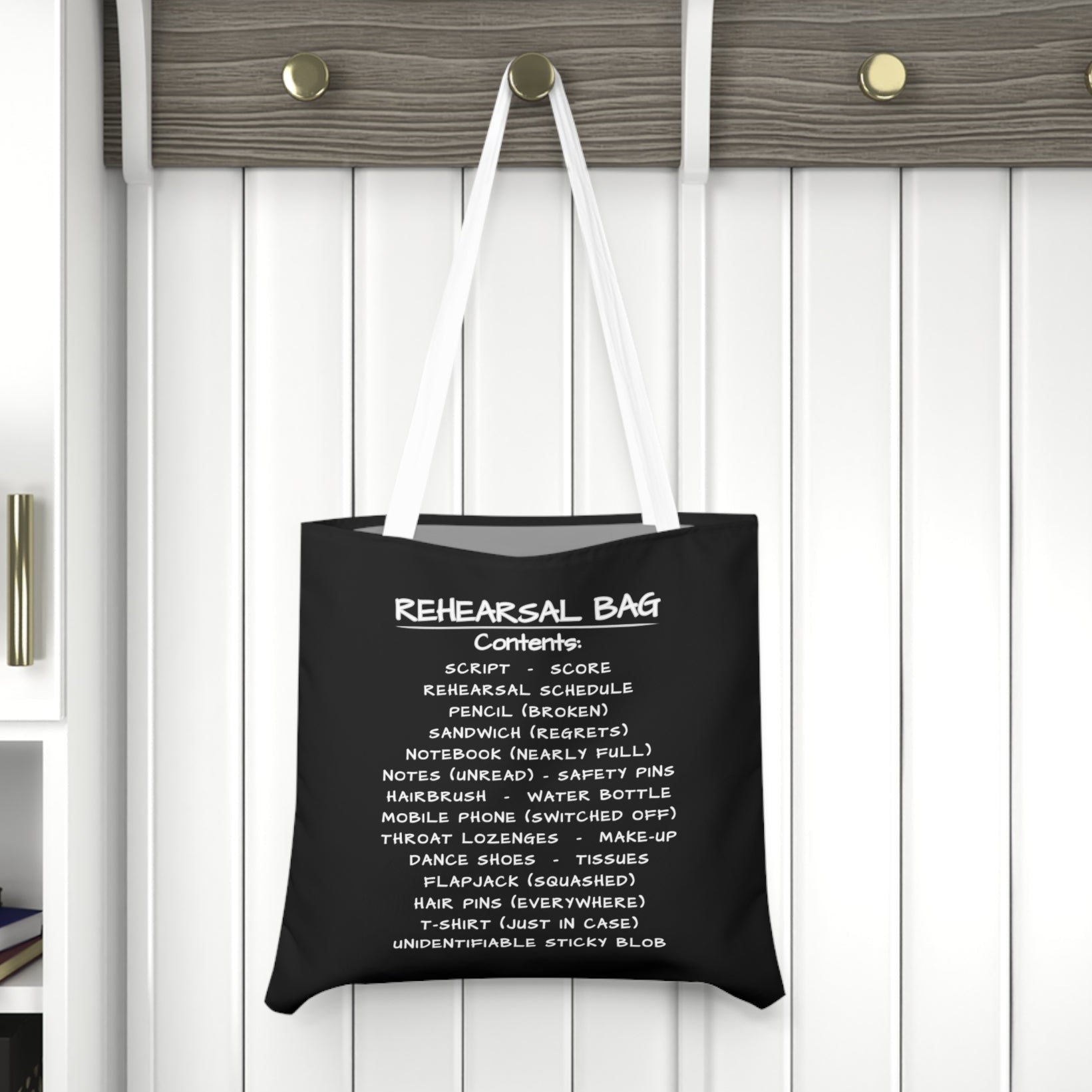 Black tote bag with white text hanging on a wooden hook against a white wall.