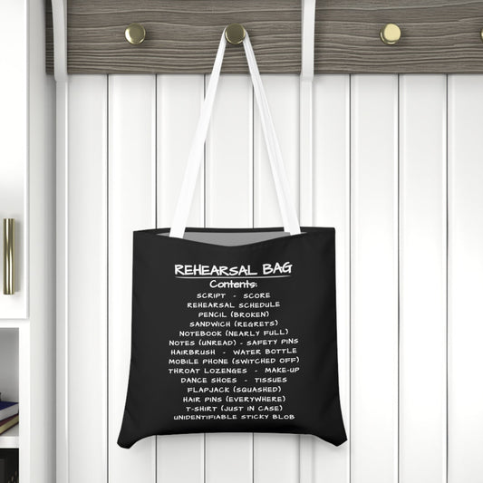 Black tote bag with white text hanging on a wooden hook against a white wall.